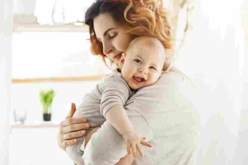 Adult holds a smiling baby against their shoulder in a bright room